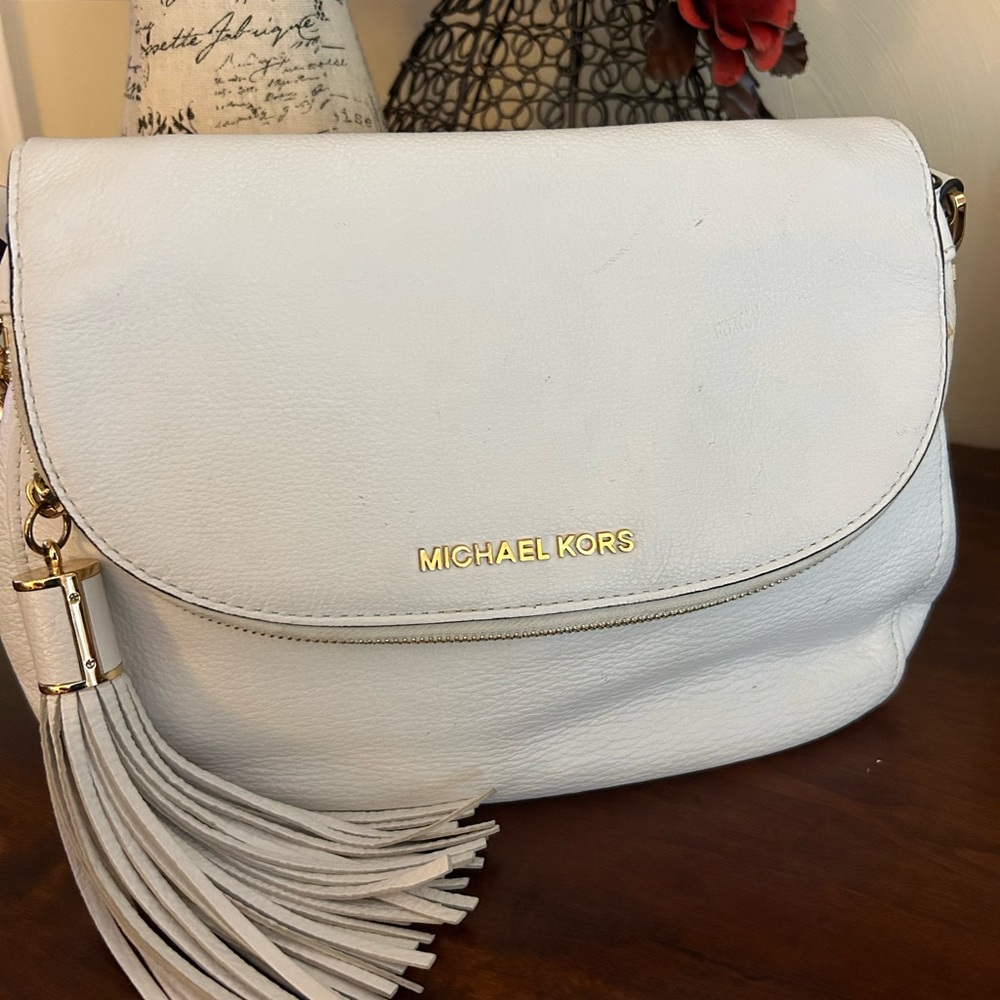 Michael Kors white purse, with zipper pockets, and tassel, gold link detail.